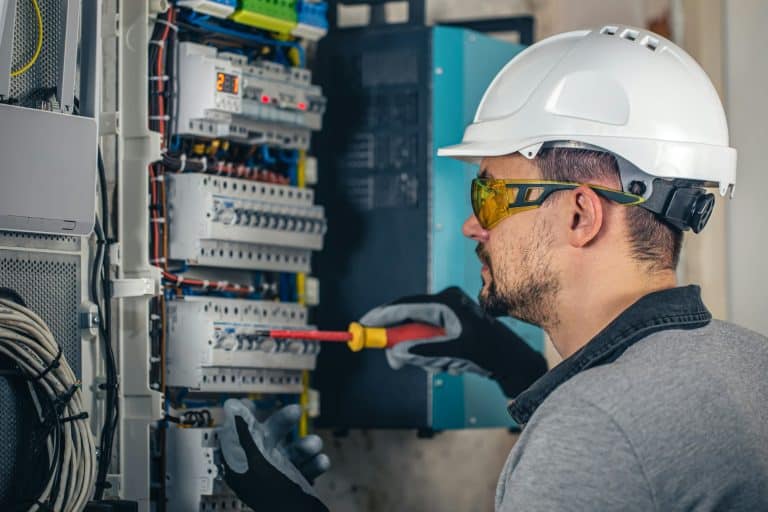 Man, an electrical technician working in a switchboard with fuses doing Emergency Electrical Services.